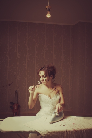 Young pretty bride with chamomile ironing bloody t-shirtの写真素材