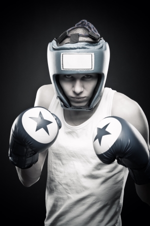 Young man in blue boxing glove posing over dark backgroundの写真素材