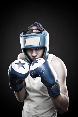 Young man in blue boxing glove posing over dark backgroundの写真素材