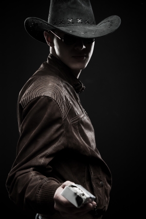 Young man in cowboy hat with cigarettes posing over dark backgroundの写真素材