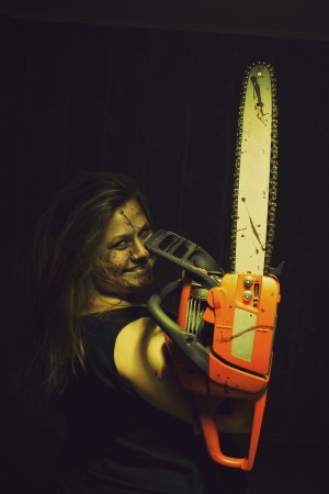 Crazy girl with bloody chainsaw posing over dark backgroundの写真素材