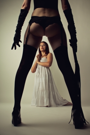 Beautiful cute model in white dress stands on knees next to legs of her dominatrix with lashの写真素材