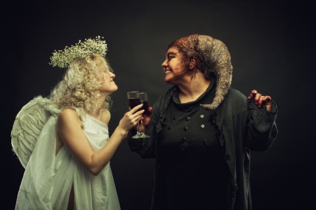 Cute little angel cheers with horned positive demon over dark backgroundの写真素材