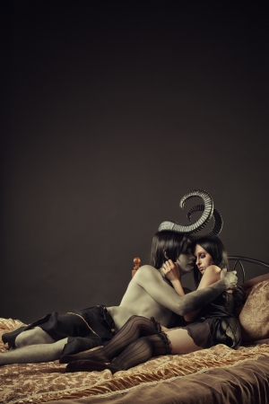 Horned devil and cute gothic girl in bedの写真素材