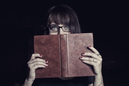 Scared student with book over dark backgroundの写真素材