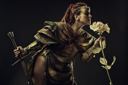 Brutal barbarian warrior with sword smelling the rose over dark backgroundの写真素材