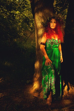 Redhead beautiful lady in green dress posing in the forestの写真素材
