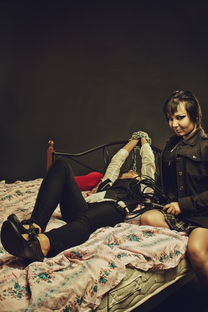 Pretty mistress with whip sitting on the bed near  bounded victimの写真素材