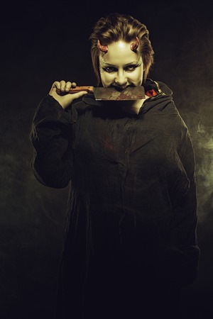 Horned pale girl with bloody butcher knife over dark backgroundの写真素材