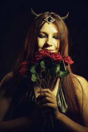 Beautiful horned girl smelling a roses over dark background.