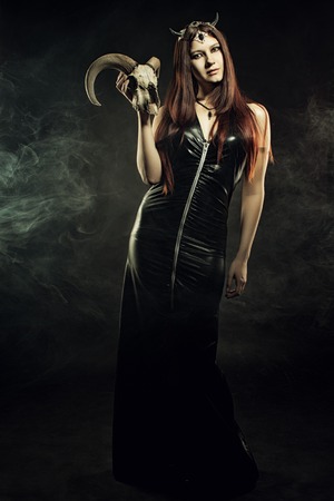 Sexy mistress in latex posing over dark background with skullの写真素材