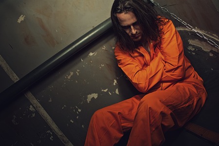 Miserable prisoner in orange clothes sitting on a bed in his cellの写真素材