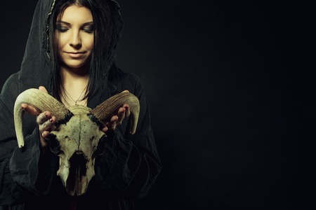Pretty young girl in hood holding skull over dark backgroundの写真素材