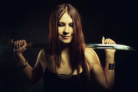 Redhead girl with sword posing over dark backgroundの写真素材