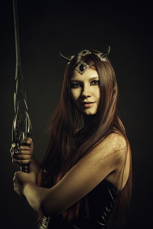 Pretty horned girl in latex posing over dark background with swordの写真素材