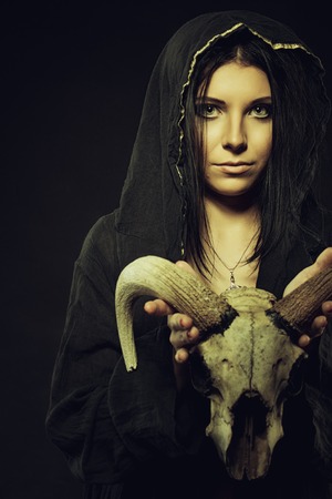 Pretty young girl in hood holding skull over dark background