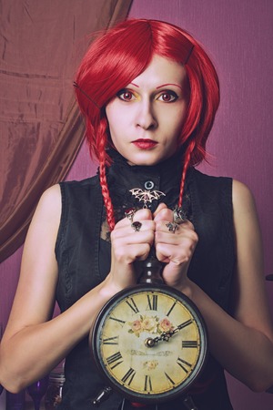 Redhead redeyed pretty girl posing with clock over violent backgroundの写真素材