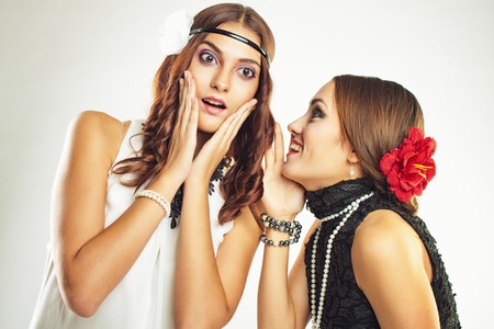 Two old-fasioned girlfriends talking over grey backgroundの写真素材