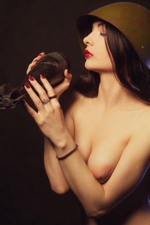 Nude girl in helmet posing over dark background with bombの写真素材