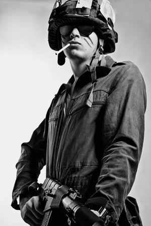 Brave young soldier in helmet posing over white background with rifle