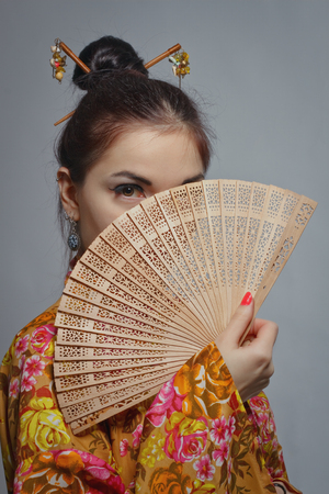 Pretty asian girl in kimono with fan posing over grey backgroundの写真素材