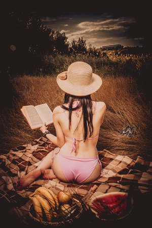 Girl in hat reading a book on a picnic. Rear view.の写真素材