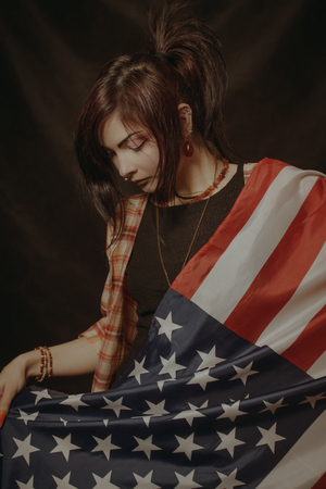 Sad asian girl posing with USA flag over dark backgroundの写真素材