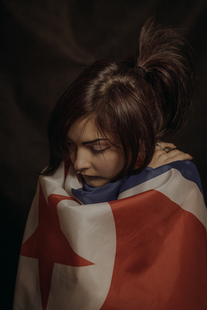 Sad asian girl wrapped in flag  of Northern Korea over dark backgroundの写真素材
