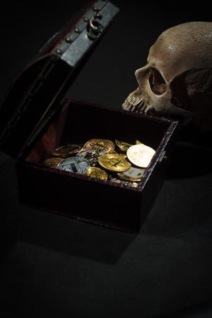 Pile of cryptocurrencies in a chest with skull over dark bacgkroundの写真素材