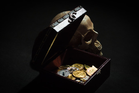 Pile of cryptocurrencies in a chest with skull over dark bacgkroundの写真素材