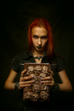 Redhead gothic girl with old grunge horrible book posing over dark backgroundの写真素材
