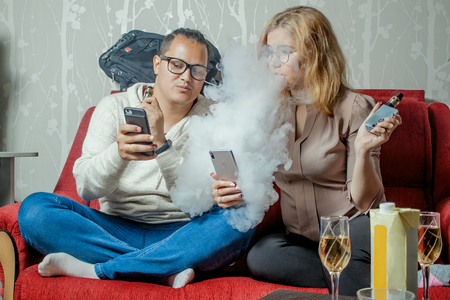Students relaxing at home, showing to eachother their phones and vapingの写真素材
