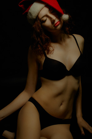 Sexy girl in Santa's hat sitting on the floor over dark backgroundの写真素材