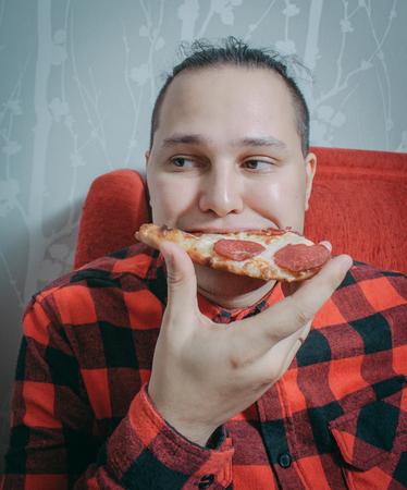 Sad guy in red shirt eating pizza at homeの写真素材