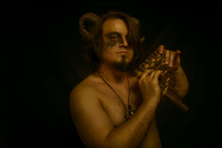 Horned faun with panflute posing over dark backgroundの写真素材