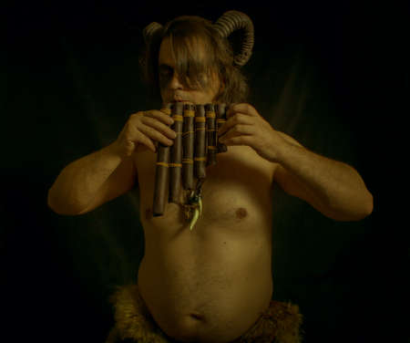 Horned faun with panflute posing over dark backgroundの写真素材