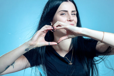 Beautiful young girl making heart sign with hands over grey background