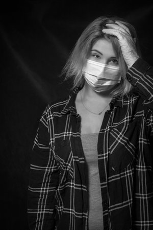 Young beautiful woman in a medical mask and gloves posing over dark backgroundの写真素材