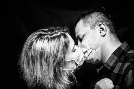 Shot of young couple in masks kissing over dark background.の写真素材