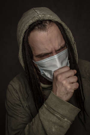 Young man in mask coughing over grey background