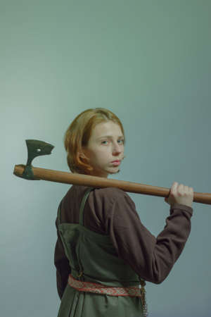 Pretty young scandinavian woman posing with axe over grey backgroundの写真素材