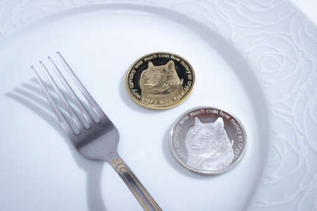 Two dogecoins in plate and fork over white background