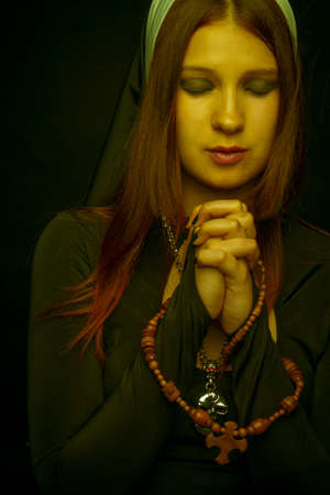 Young praying nun over dark background