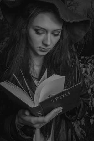 Cute pretty girl in witch hat posing with spellbook outdoorsの写真素材
