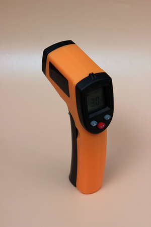 Infrared thermometer (thermometer gun) for measuring temperature over yellow background.