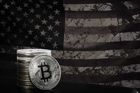 One silver bitcoin and stack of bitcoins over grunged USA flag