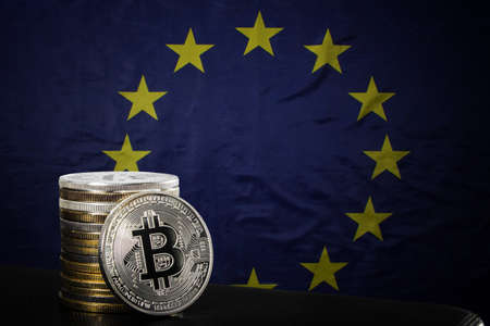 One silver bitcoin and stack of bitcoins over EU flagの写真素材