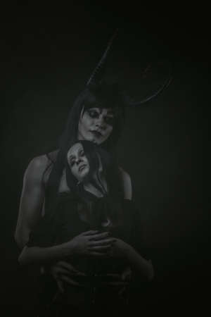 Horned demon embrasing cute gothic girl over dark background