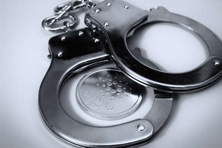 Cardano coin and handcuffs. Grayscale image.