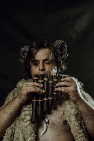 Horned faun with panflute posing over dark backgroundの写真素材